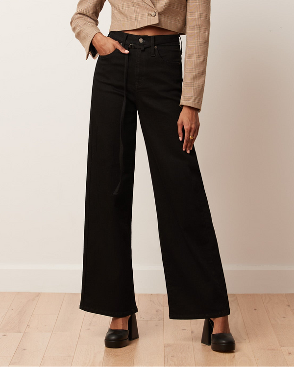 Woman wearing a beige blazer and black pants against a plain background