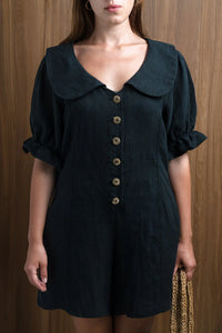 Woman wearing black linen dress with large collar and wood buttons, holding woven bag