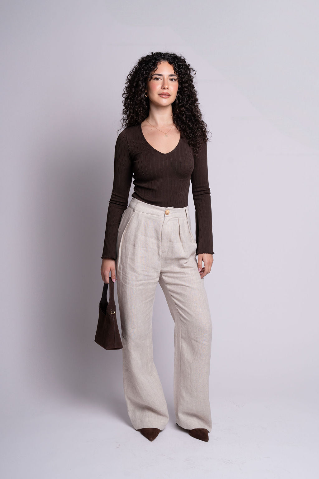 Woman wearing a brown top and beige pants against a plain background