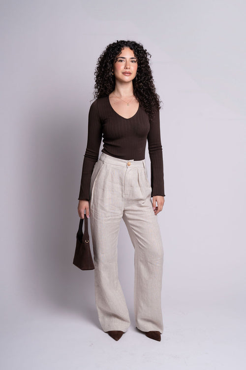 Woman wearing a brown top and beige pants against a plain background