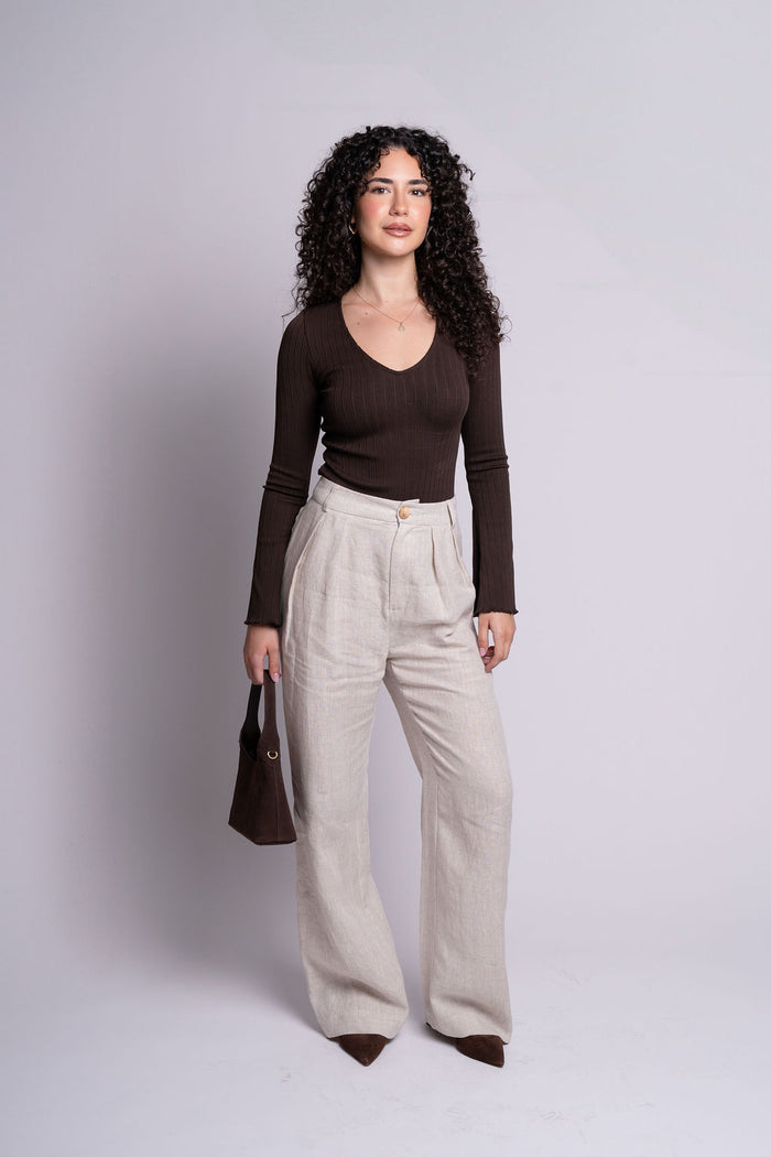 Woman wearing a brown top and beige pants against a plain background