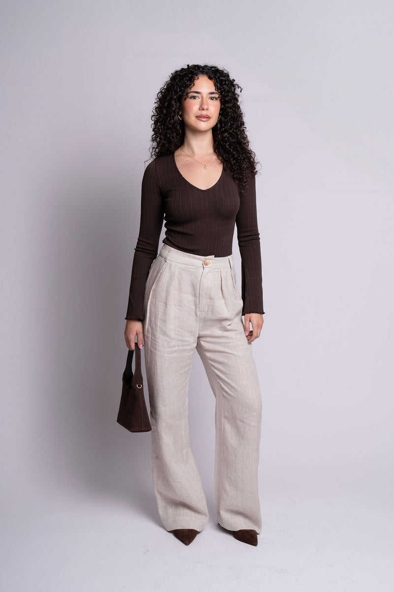 Woman wearing a brown top and beige pants against a plain background