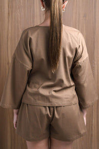 Woman in brown loungewear set with loose top and shorts, back view, wood background