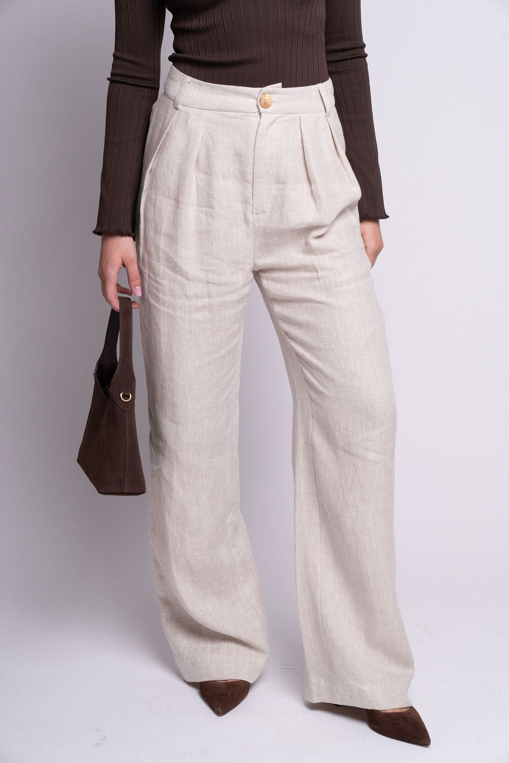 Person wearing beige pleated pants and a brown top on a white background