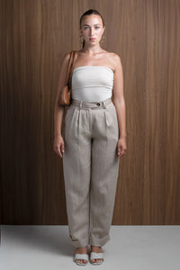 Woman in beige strapless top and high-waisted linen pants with brown shoulder bag, wood backdrop