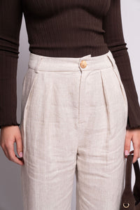 Person wearing a brown ribbed sweater and beige pleated pants against a plain background