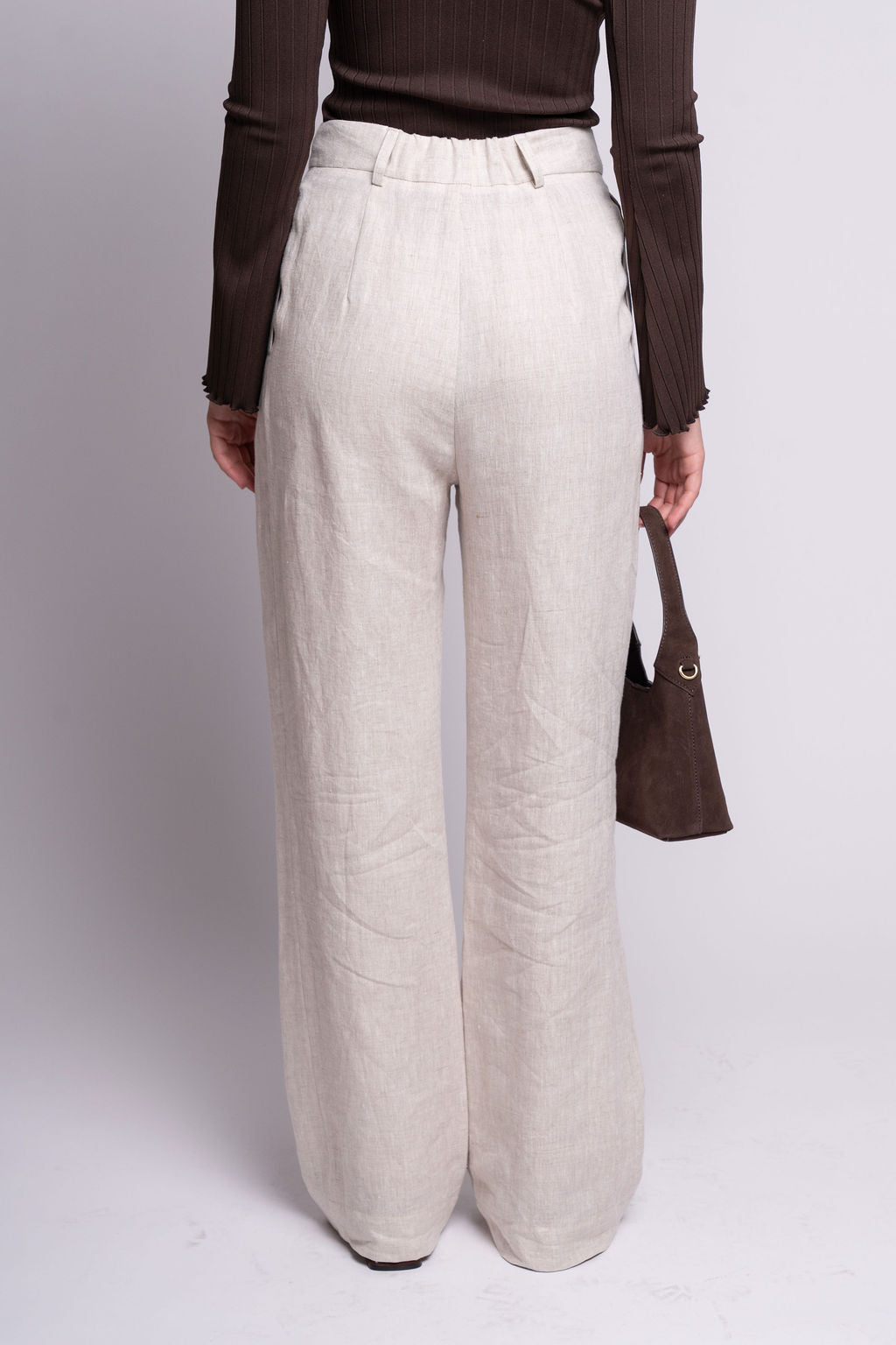 Person wearing light-colored wide-leg pants and a brown top on a white background