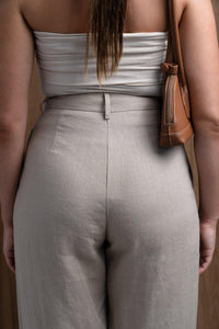 Back view of woman in high-waisted beige linen pants, white tube top, brown leather bag