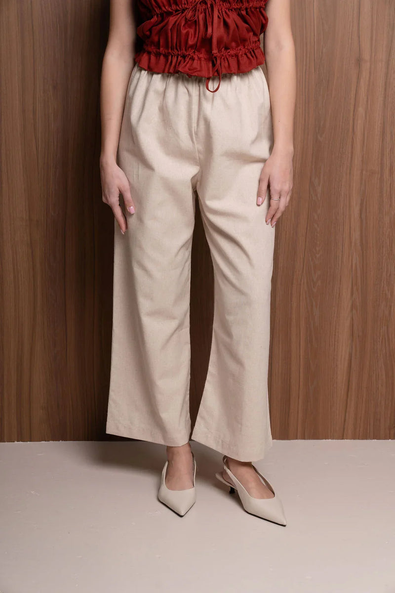 Woman wearing beige wide-leg pants and pointed heels, red ruched top, wooden background