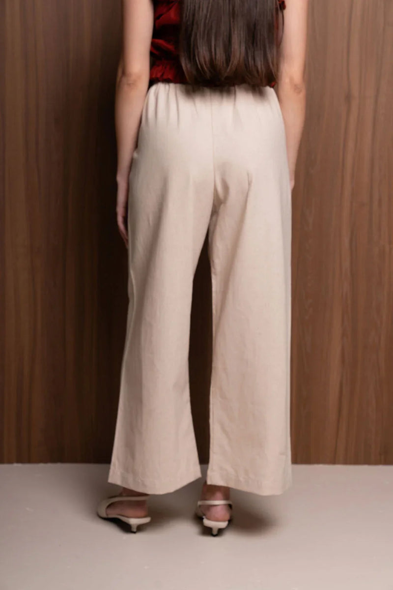 Back view of woman wearing beige wide-leg pants and white sandals, wood panel background