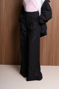 Person wearing black pinstripe pants and a cropped jacket against a wooden background