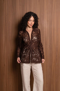 Woman in brown lace long-sleeve blouse and beige pants standing by wood panel wall