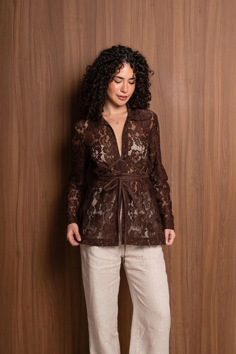 Woman in brown lace long-sleeve blouse and beige pants standing by wood panel wall