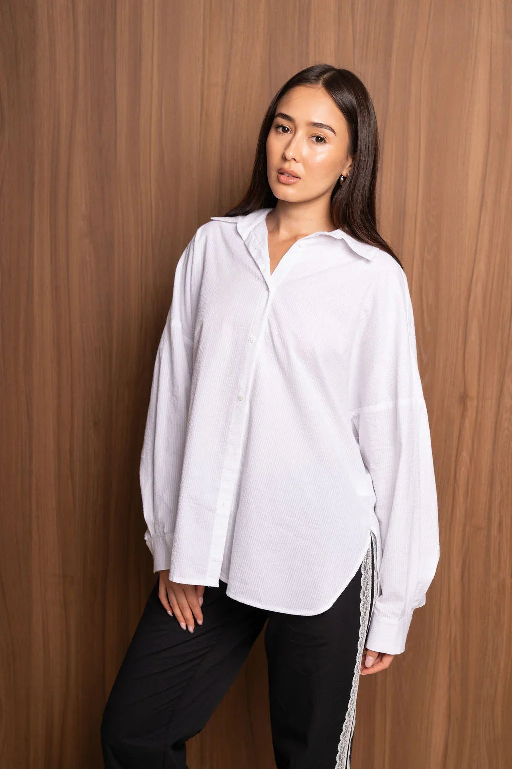 Woman wearing oversized white button-up shirt and black pants with lace trim, wood background