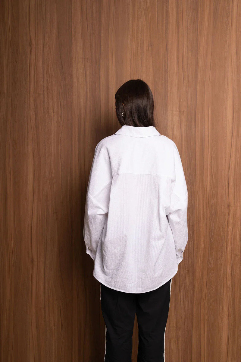 Person in white textured shirt and black pants standing against a wood panel wall