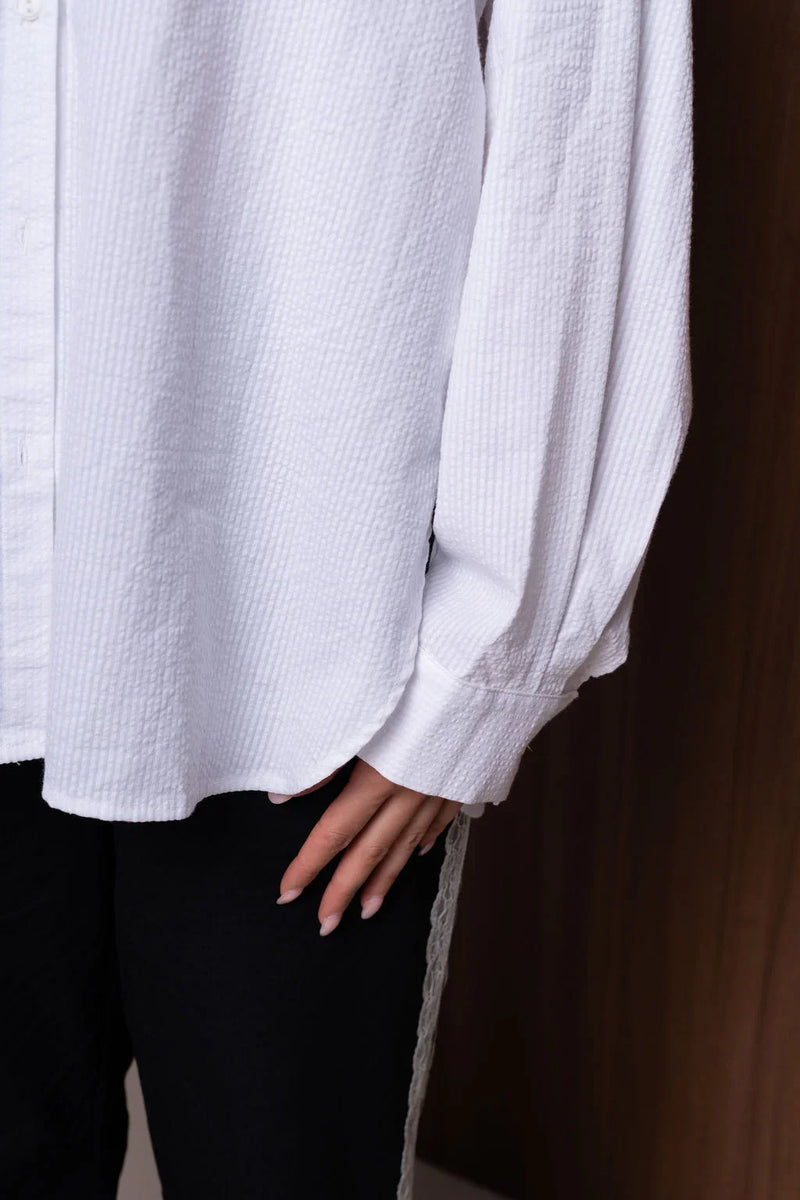 Textured white button-up shirt with long sleeves, hand resting on black pants