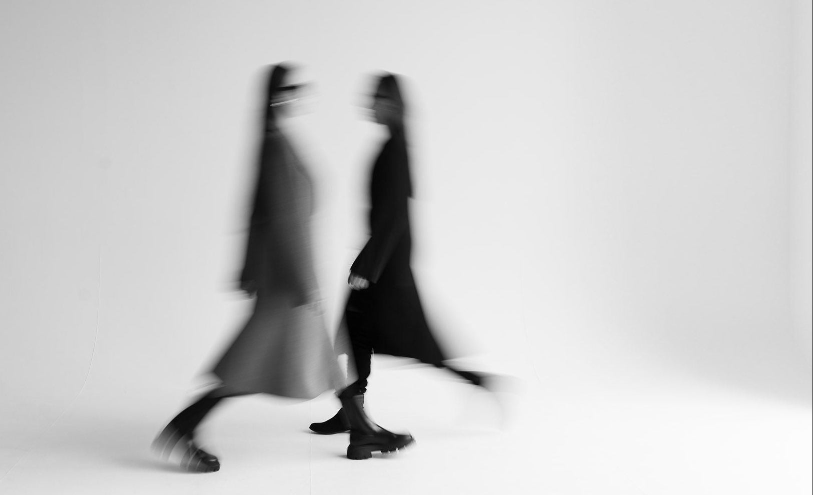 Two blurred figures walking on a white background