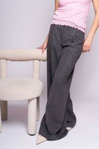 Person wearing gray striped pants and a pink top sitting on a chair against a plain background
