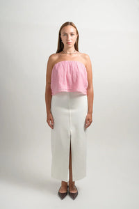 Woman in studio wears pink strapless top and white midi skirt with front slit