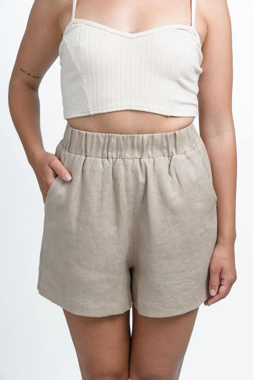 Woman wearing beige linen shorts and ribbed crop top against white background