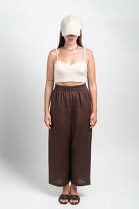 Woman wearing cream crop top, brown wide-leg pants, beige cap, and sandals in studio