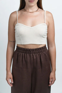Woman wearing a beige ribbed crop top, brown high-waisted pants, and gold choker necklace