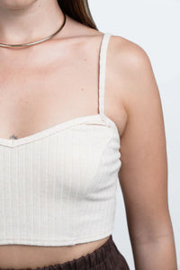 Woman wearing ribbed cream crop top, brown pants, and gold choker necklace