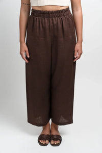 Woman wearing brown wide-leg linen pants and dark sandals on white background