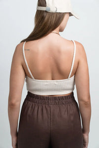 Woman in beige ribbed crop top, brown high-waisted pants, and tan cap, seen from back