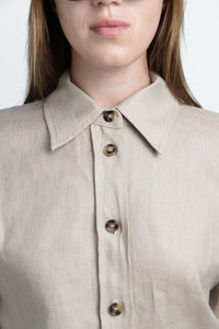 Closeup of woman in beige linen button-up shirt with brown buttons and pointed collar