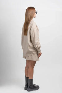 Woman in beige linen shirt and shorts, black boots, side view on white background