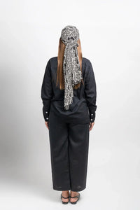 Woman in black outfit with geometric patterned headscarf, photographed from behind