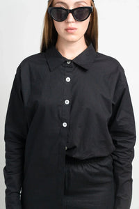 Woman in black button-up shirt and black cat-eye sunglasses against white background