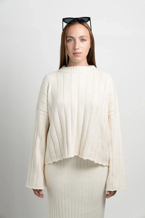 Woman wearing cream ribbed knit sweater and skirt set with black sunglasses indoors