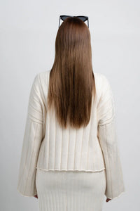 Woman with long brown hair, wearing cream ribbed knit sweater and skirt, back view