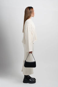 Woman in cream knit sweater and skirt with black bag and chunky boots, side view