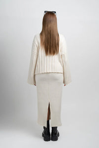 Back view of woman in cream ribbed knit sweater and skirt set with chunky black boots