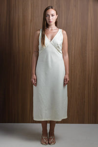 Woman in cream midi dress with V-neck, strappy heels, standing against wood panel background