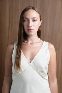 Woman in cream dress with pearl necklace, tattoo, and straight hair against wood background