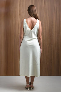 Woman in white sleeveless midi dress with deep V-back, standing against wood panel wall