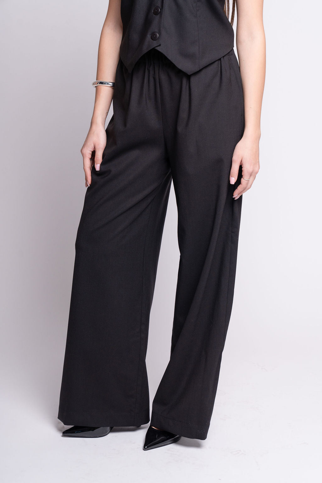 Person wearing a black outfit with wide-leg pants on a light gray background
