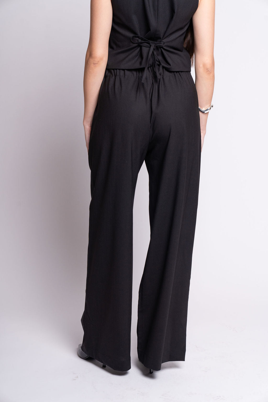 Person wearing a black outfit with wide-leg pants on a light gray background