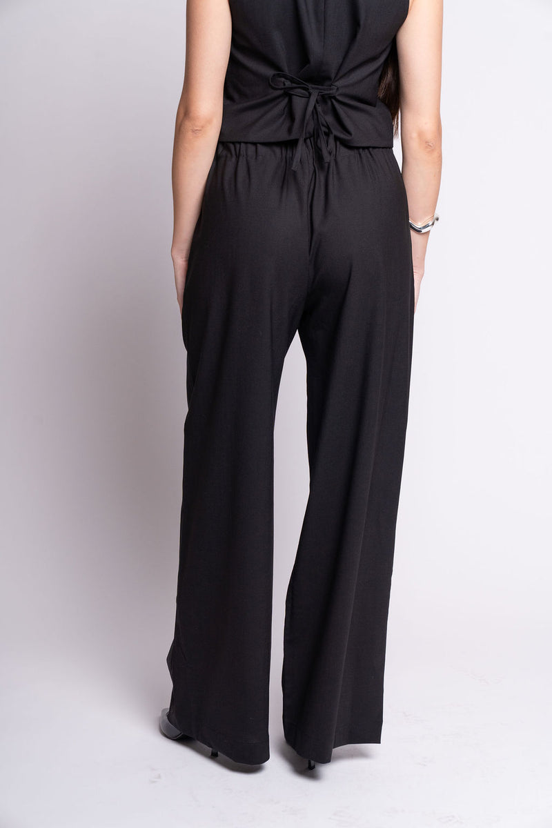 Person wearing a black outfit with wide-leg pants on a light gray background