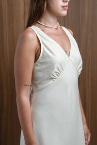 Woman in sleeveless ivory dress with pearl necklace and tattoo, wood background