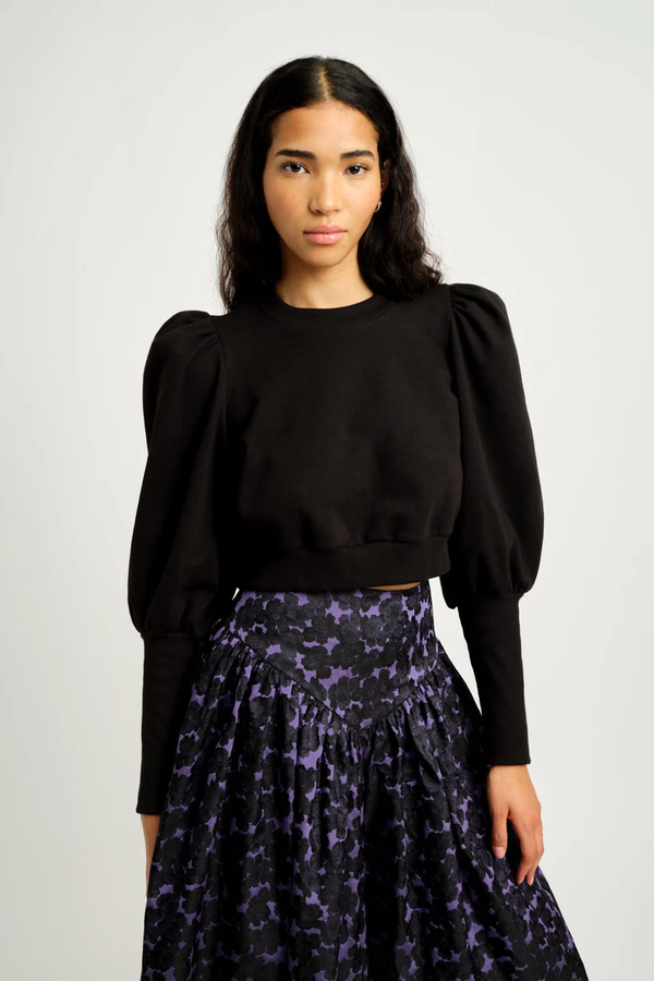 Woman wearing a black top and patterned skirt against a white background