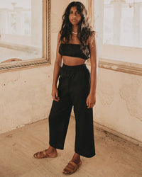 Woman modeling black linen crop top and wide-leg pants in rustic indoor setting