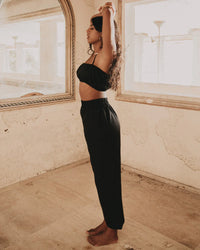 Woman wearing black linen pants and matching top stretching in rustic room with mirror