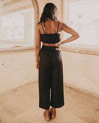 Woman wearing black linen crop top and wide-leg pants in a sunlit rustic room