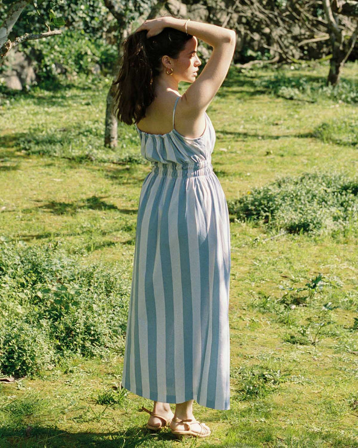Woman in a blue and white striped dress standing in a grassy field.