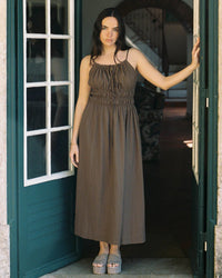 Woman in sleeveless mocha cotton maxi dress standing in doorway, platform sandals, natural light